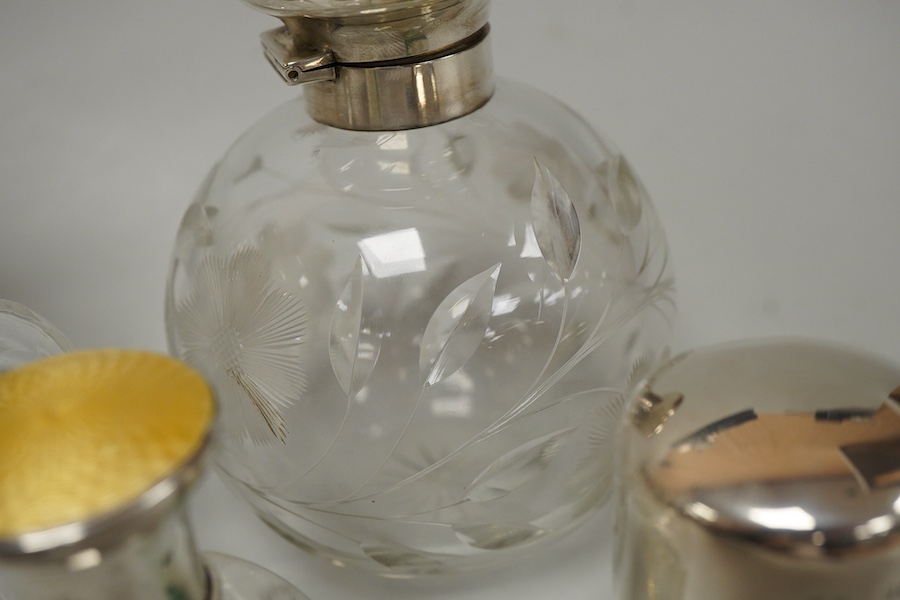 A collection of five silver mounted glass scent bottles to include one with guilloche enamel inset top, a Victorian example hallmarked for Chester 1897 and a cut glass example with mother of pearl top, London 1922, large